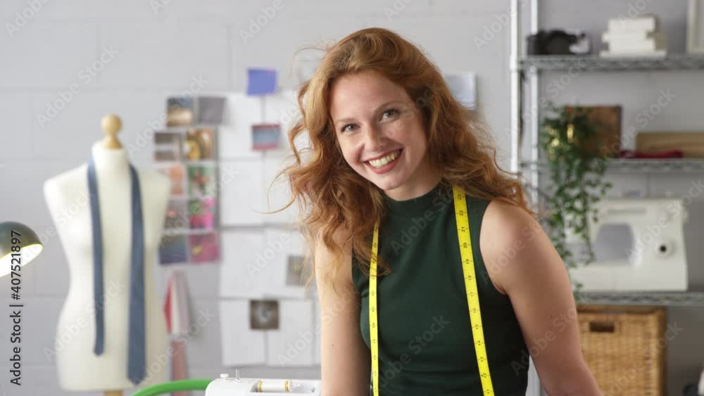 Portrait of female clothes designer with tape measure around neck sitting on desk in fashion studio - shot in slow motion Portrait of female clothes designer with tape measure around neck sitting on desk in fashion studio - shot in slow motion