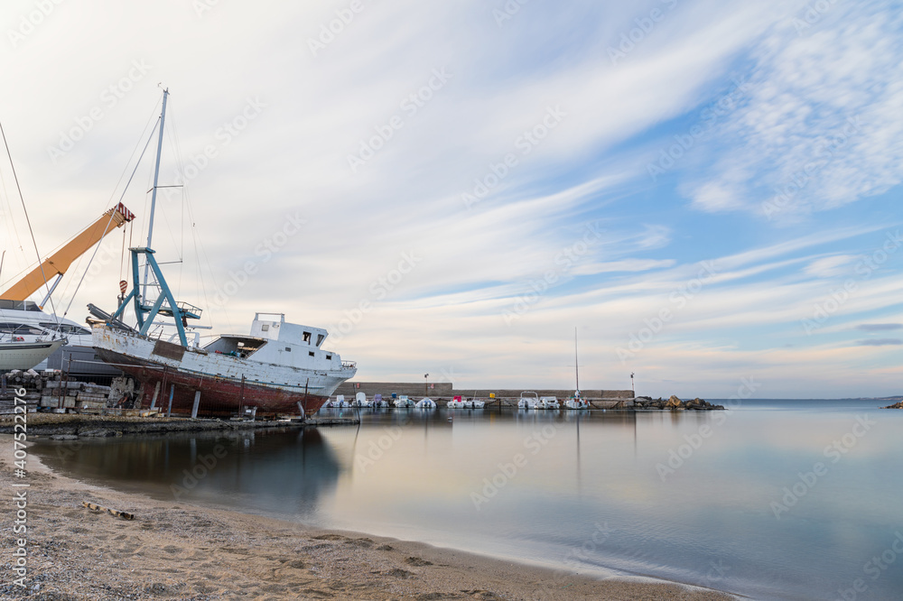 Port in the city of Gallipoli in Puglia, Italy.  A large fishing boat with red and white color.  A blue sky with scattered clouds, calm and clear sea with a typical southern Italian beach.