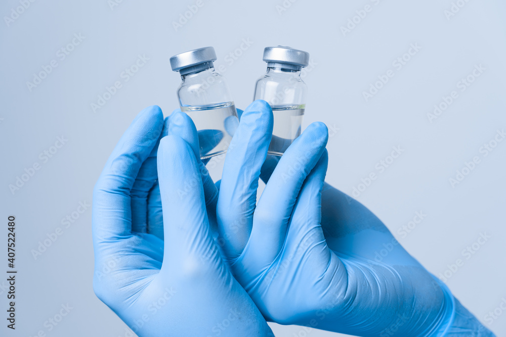 Close-up covid-19 Vaccination. 2 doses of coronavirus vaccine. Woman in blue medical gloves holding medication. Close-up covid-19 Vaccination. 2 doses of coronavirus vaccine. Woman in blue medical gloves holding medication.