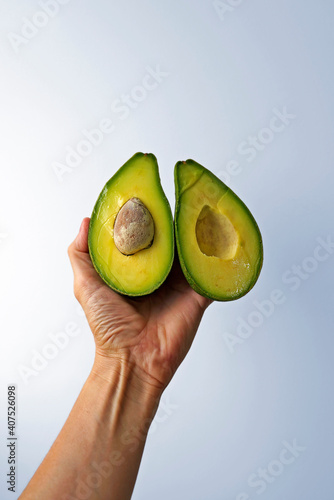 Halves of an avocado on hand in a bright background