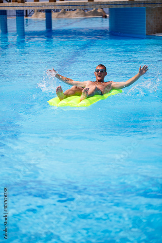 A young man bathes in the pool on a yellow inflatable mattress. Relax in the bright sun on vacation. Happy successful guy