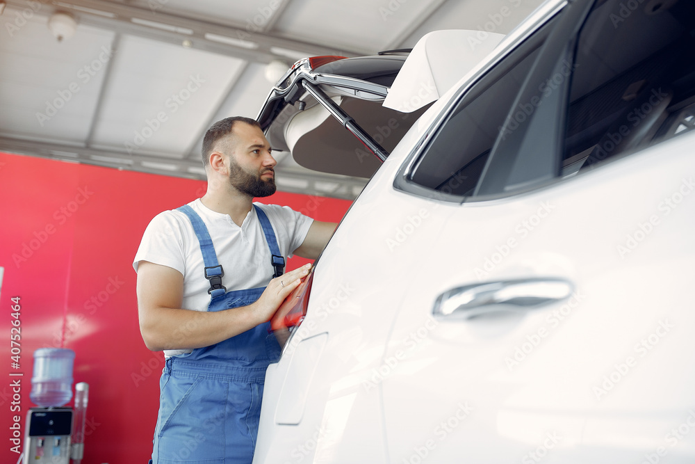 Wrker in a car salon. Expert checks the car. Man in a blue uniform. Wrker in a car salon. Expert checks the car. Man in a blue uniform.