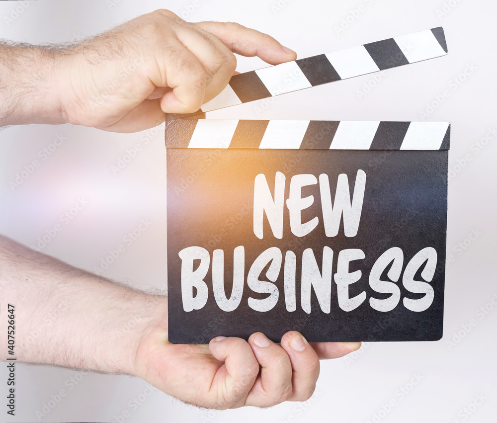 Obraz premium On a white background, a man holds a clapperboard in his hands on which it is written - NEW BUSINESS
