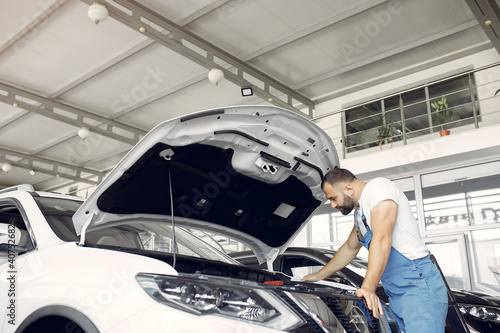 Wrker in a car salon. Expert checks the car. Man in a blue uniform. photo