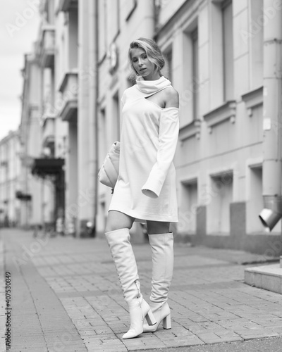 Elegant young female model with makeup and hairstyle standing and posing at city street. Autumn fashion