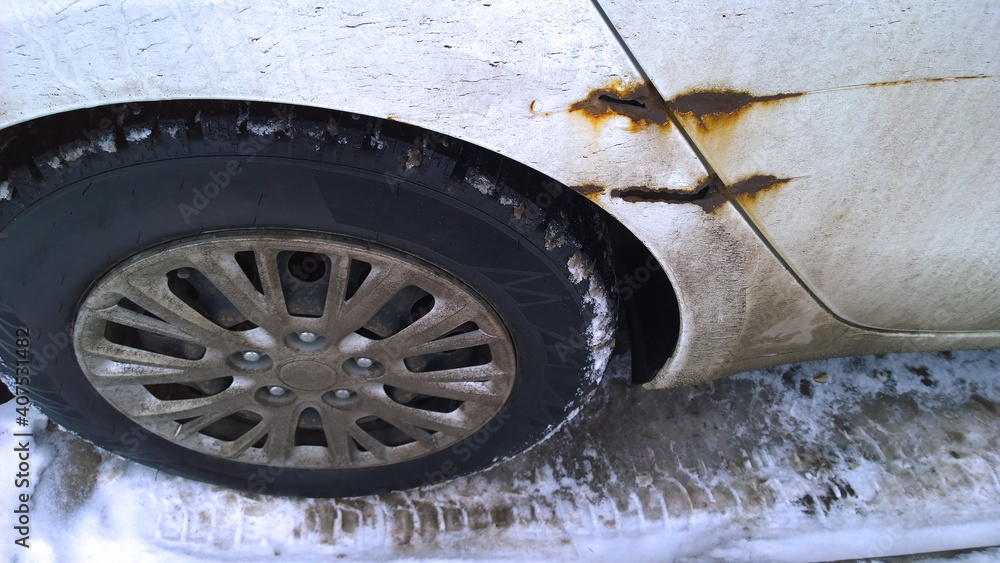 Sheet metal corrosion over wheel of old white car. Rusty messy surface. Damaged grunge dirty texture from road salt. Rust background. Protecting automobile concept. Resistance test. Paint work. Snow.