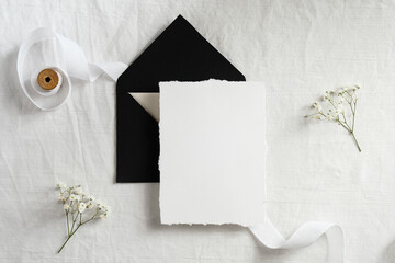 Wedding invitation template. Black envelope and blank card on textile background with ribbon and flowers. Elegant wedding flat lay composition.