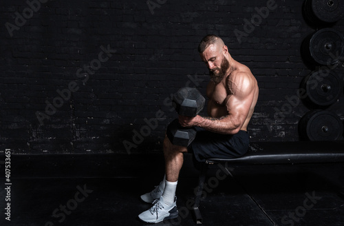 Fototapeta Young active strong sweaty fit muscular man with big muscles sitting on the benc
