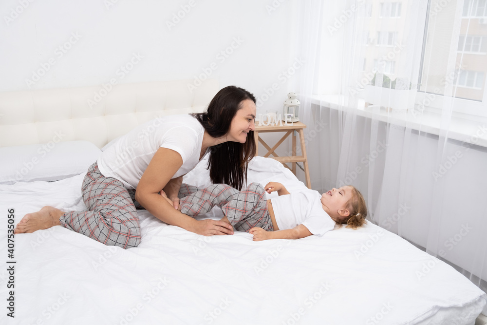 adult mother is tickling her little active daughter in bed at home, leisure activity with children. adult mother is tickling her little active daughter in bed at home, leisure activity with children.