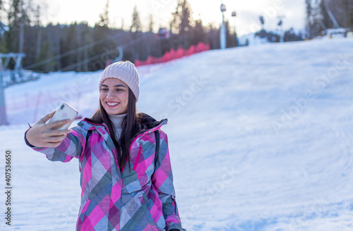 Portrait of a young woman in winter clothes on the ski-run taking a selfie.