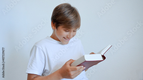Teenage boy wearing white t-shirt smiling reading heavy book