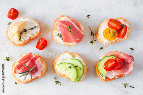Assortment of cream cheese crostini hors d'oeuvres with a variety of toppings. Above view on a white marble background. Party food concept.