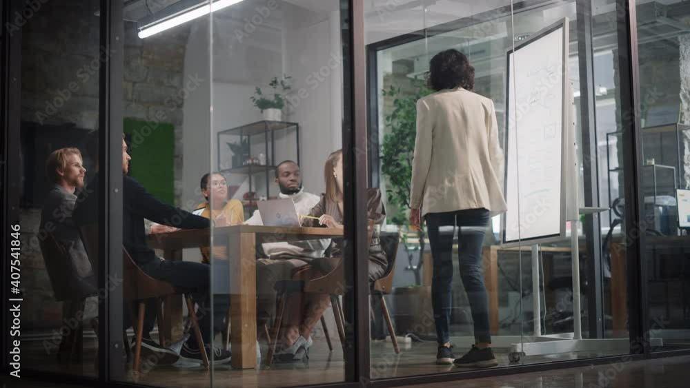 Project Manager Makes a Presentation for a Young Diverse Creative Team in Meeting Room in an Agency. Colleagues Sit Behind Conference Table and Discuss Business Development, User Interface and Design. Project Manager Makes a Presentation for a Young Diverse Creative Team in Meeting Room in an Agency. Colleagues Sit Behind Conference Table and Discuss Business Development, User Interface and Design.