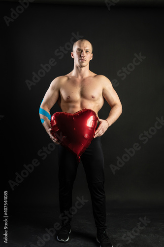 Athletic man holding a red heart, a naked balloon in his hand for a day of velentin pumped up, bodybuilder romantic. lover guy LGBT. In the studio on a black background Joyful looking at the camera
