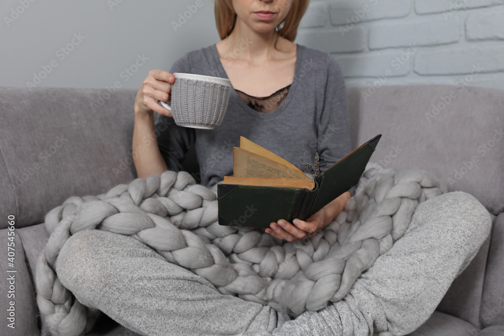 Obraz premium Cozy Woman covered with warm soft merino wool blanket reading a book. Relax, comfort lifestyle.