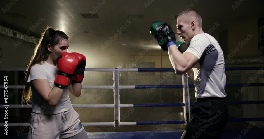 Trainer and athlete girl train punches in boxing gloves confidently and professionally in the ring night training Trainer and athlete girl train punches in boxing gloves confidently and professionally in the ring night training
