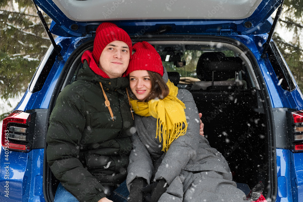Romantic young hipster couple hugging while sitting in car trunk under falling snow. Love, valentines and holiday concept. Kiss and hug. Valentines day celebration and happiness concept Romantic young hipster couple hugging while sitting in car trunk under falling snow. Love, valentines and holiday concept. Kiss and hug. Valentines day celebration and happiness concept