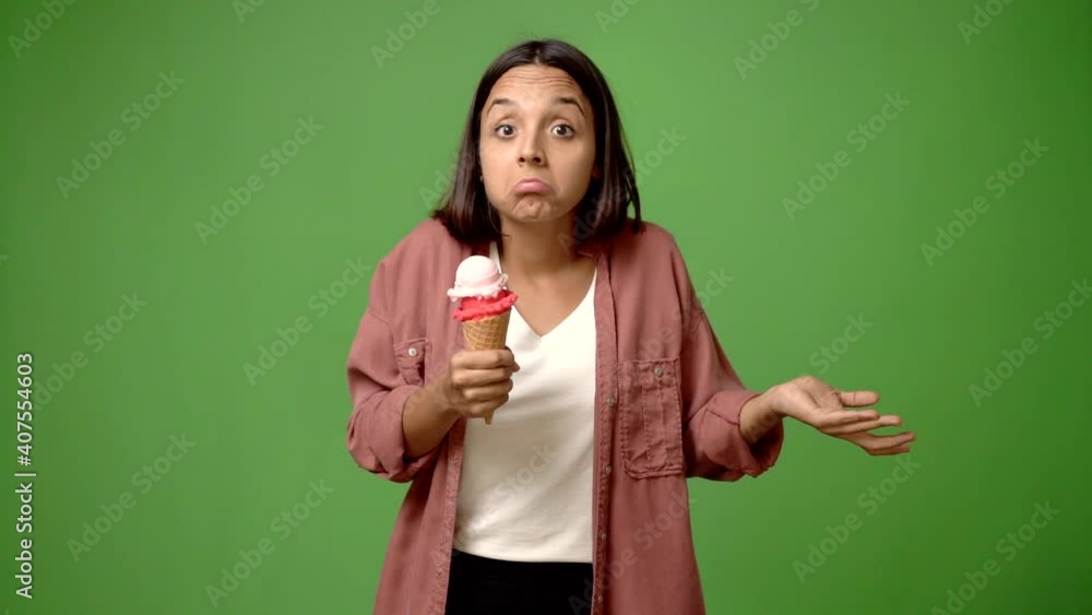 Young woman holding a cornet ice cream making unimportant and doubts gesture while lifting the shoulders and the palms of the hands