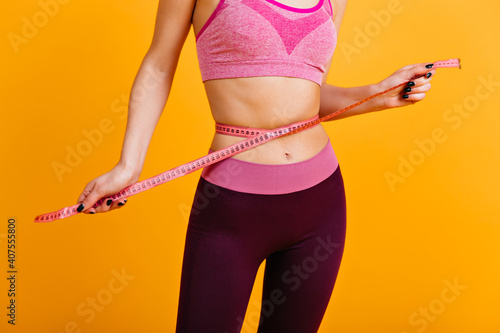 White woman posing with measure tape on her waist. Sporty girl wears pink sportswear.