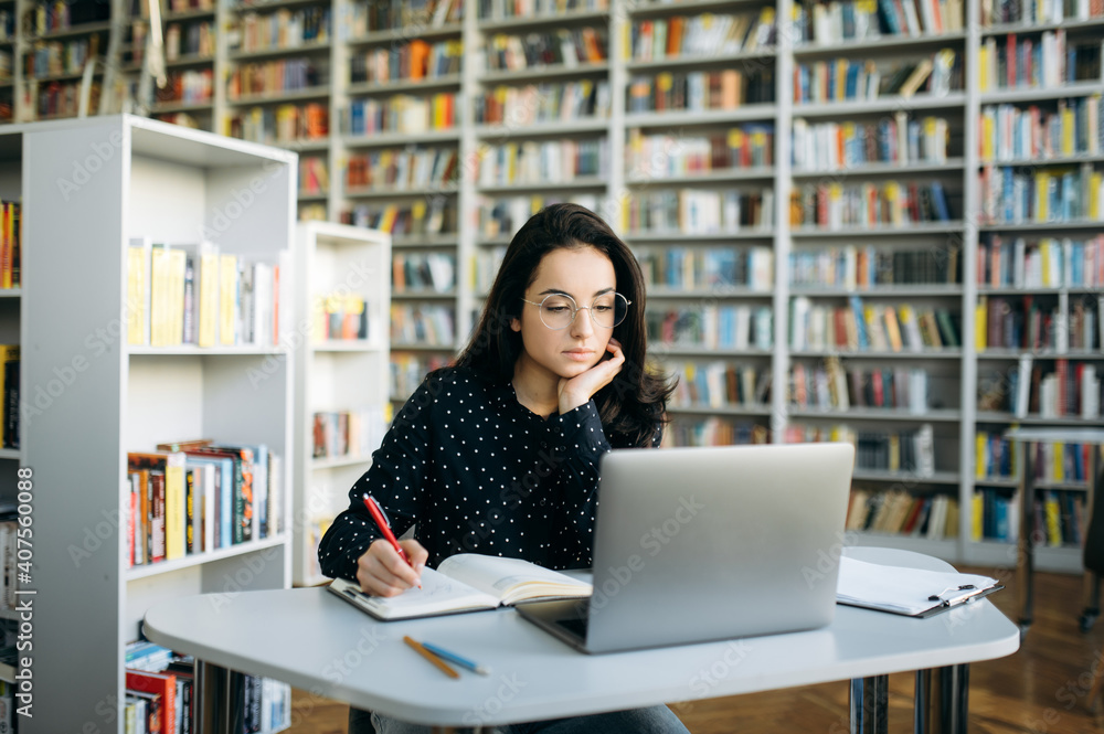 Concentrated caucasian woman sit at the desk, using laptop. Focused young adult female freelancer planning a business project, or studying online Concentrated caucasian woman sit at the desk, using laptop. Focused young adult female freelancer planning a business project, or studying online