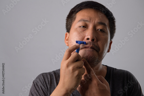 Portrait of men mustache shaving on grey background, Men's health face care concept. Asian man is shaving in dark.