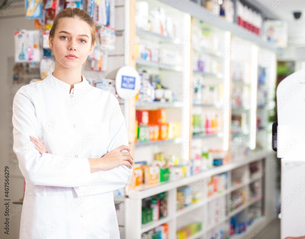 Cheerful woman pharmacist standing with arms crossed in interior of pharmacy. High quality photo