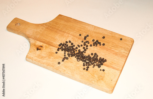 Black pepper peas scattered on a light wooden board, on a white background photo