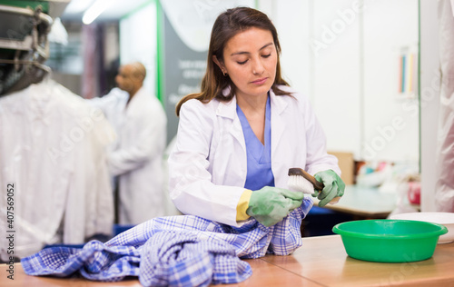 Portrait of confident dry cleaning employee at work  woman cleaning shirt with brush