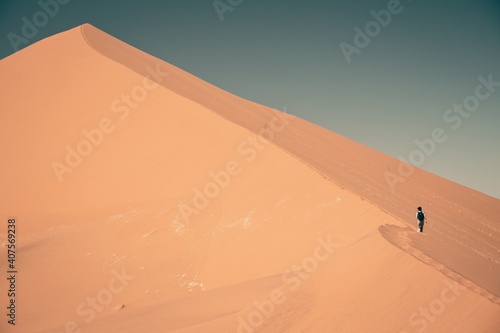 Hiker climbing huge sand dune mountain in desert