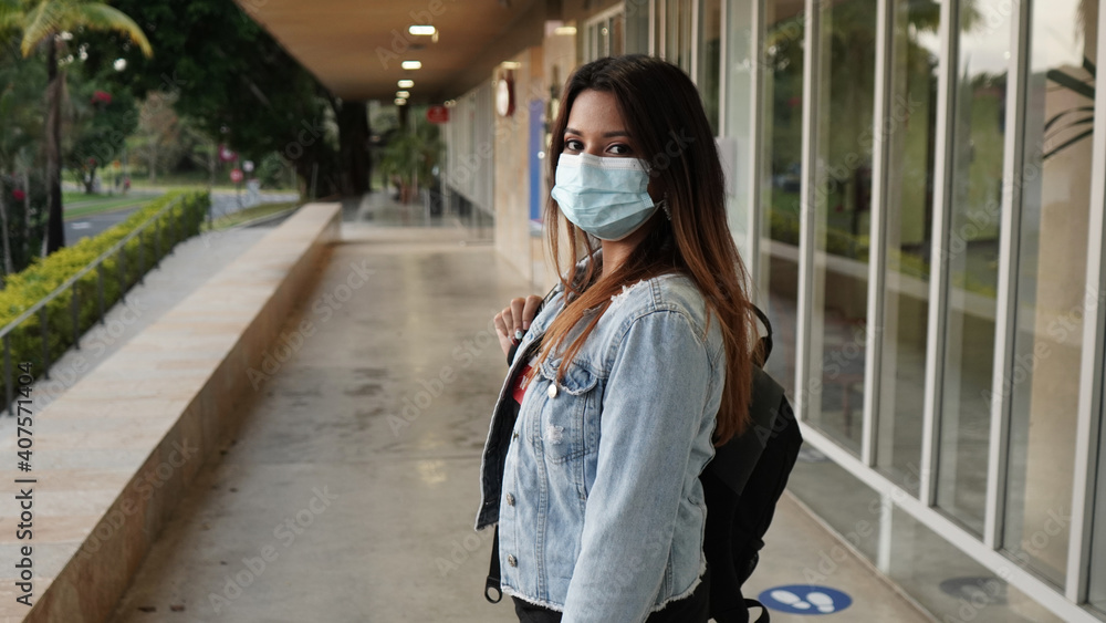 beautiful girl with a backpack on her back at school or college wearing a face mask to prevent virus in the new normal