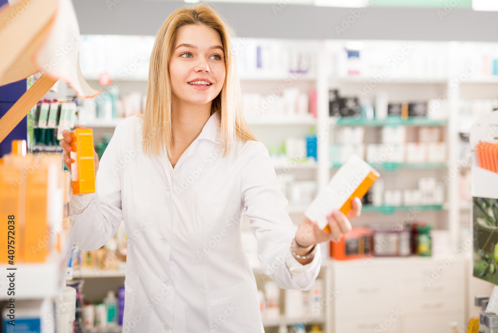 Portrait of diligent smiling pleasant positive female druggist in white coat working in pharmacy. High quality photo