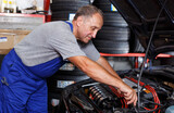 Professional mature man car mechanician repairing car in auto repair shop..