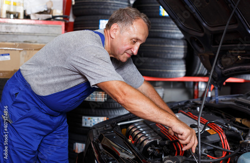 Professional mature man car mechanician repairing car in auto repair shop..