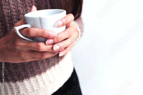 Woman's hands in sweater holding cup of coffee.