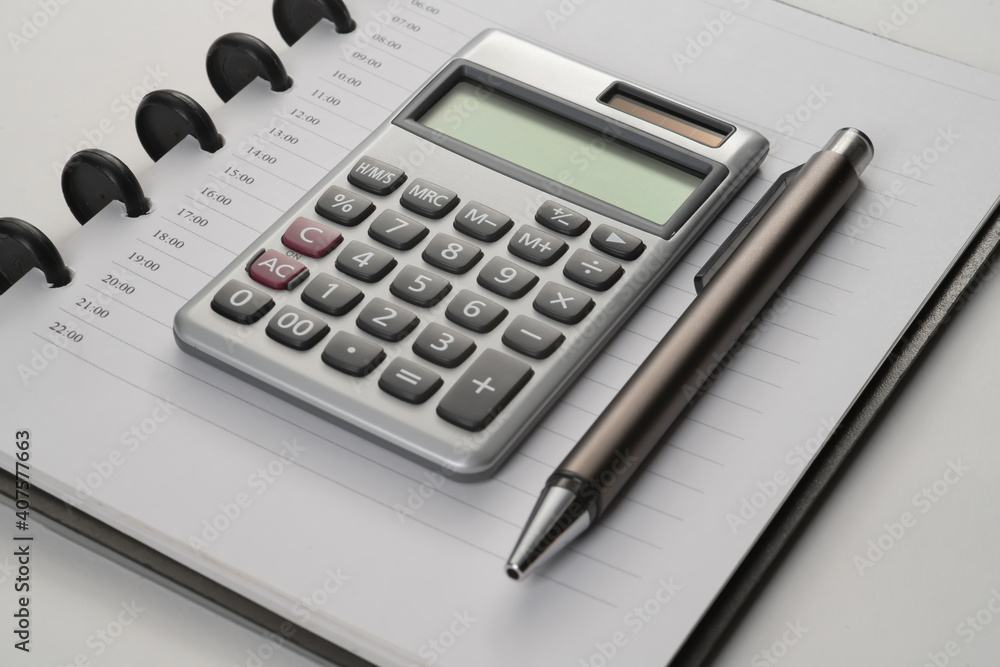 close up of notebook with pen and calculator on white flat surface close up of notebook with pen and calculator on white flat surface
