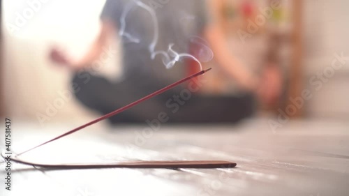 Steaming incense stick close-up on the floor and yogi in the background