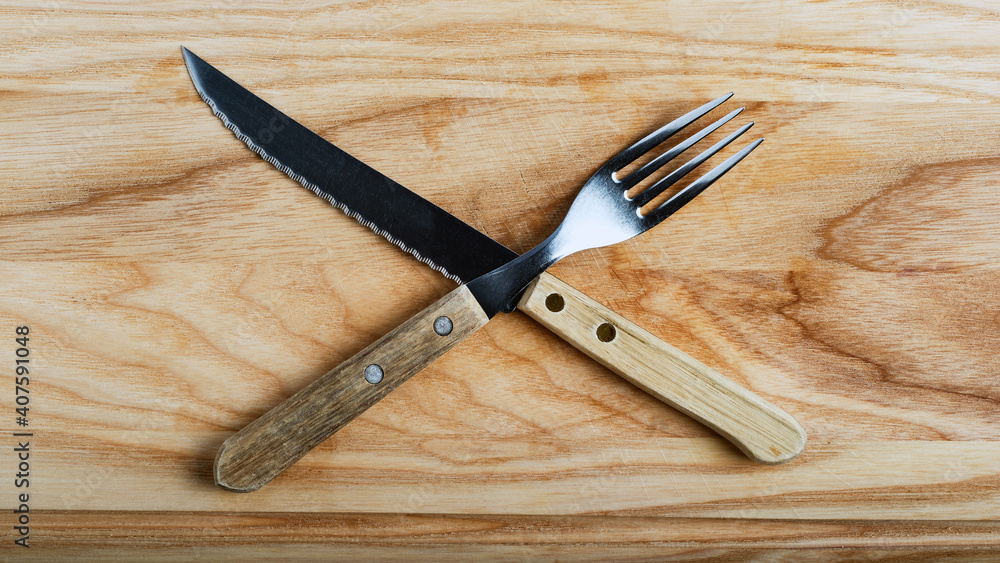 knife and fork stacked in cross on light wood board, top view, banner concept, close-up knife and fork stacked in cross on light wood board, top view, banner concept, close-up
