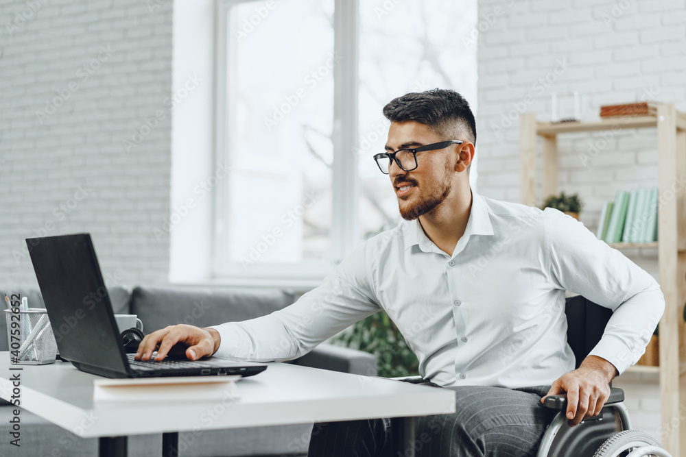 Positive disabled young man in wheelchair working in office Positive disabled young man in wheelchair working in office