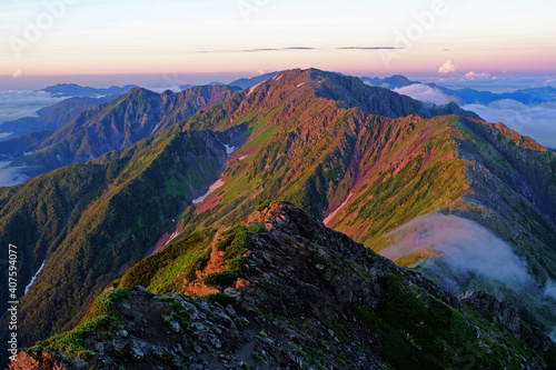 南アルプス 北岳の山頂から 朝日が差し込み朝焼けする間ノ岳方面の稜線を眺める