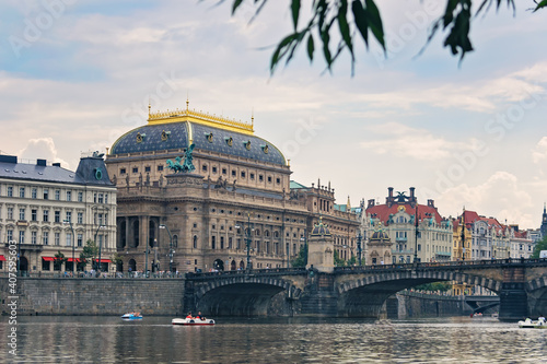 Panoramic view with the Vltava river, a stone old bridge and historical buildings in the center of Prague (Czech Republic) on a sunny summer day. Blue sky with white cumulus clouds.