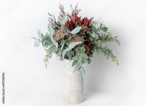 Beautiful flower arrangement of mostly Australian native flowers, including Silvan Reds, Queen Anne's Lace, Wattle foliage and Eucalyptus leaves, in a ceramic white vase, with a white background Fototapeta