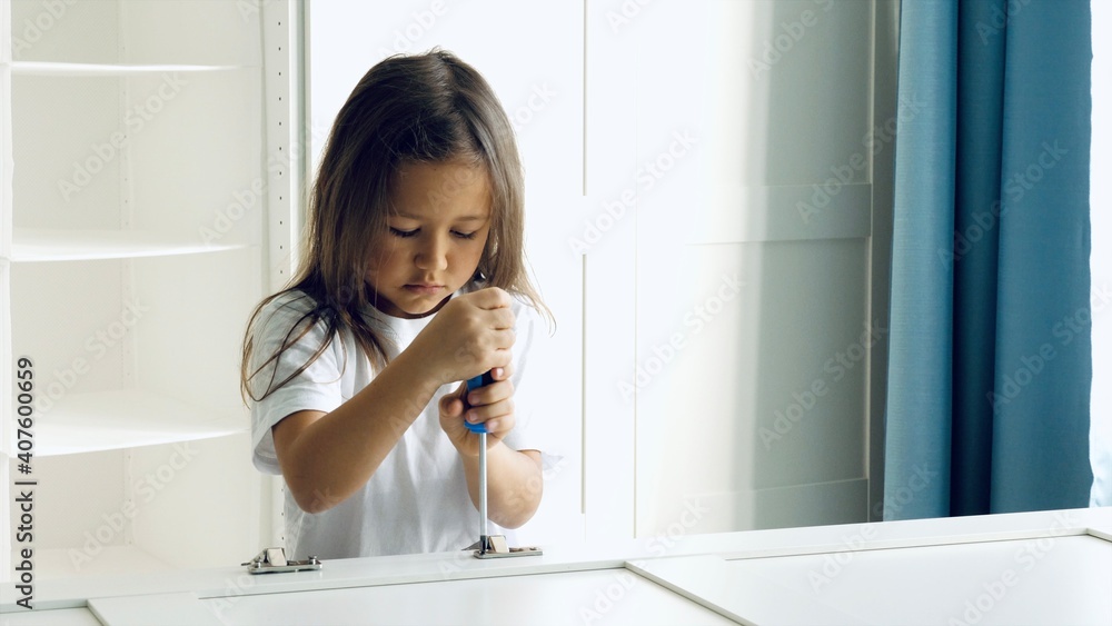 Furniture assembly process. A little child girl is installing the hinges on the doors of the closet via screwdriver Furniture assembly process. A little child girl is installing the hinges on the doors of the closet via screwdriver
