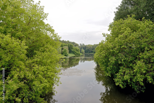 View of a pond with trees with green foliage on the banks and reflections of trees in the water. Summer landscape with pond and trees