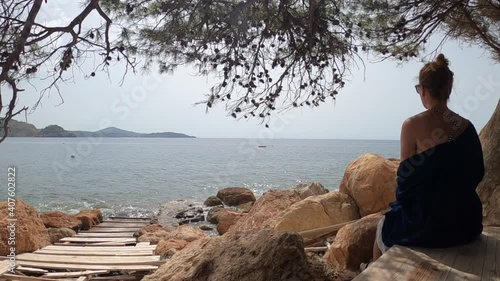 mujer sola sentada mira  al mar ,disfrutando de la vista en una roca