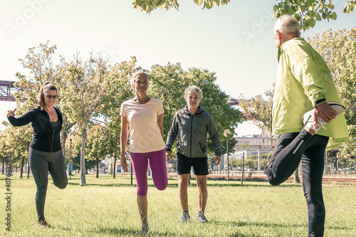 Group of retired active mature people wearing sports clothes, doing morning exercise on park grass. Retirement or active lifestyle concept