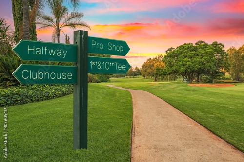 Golf course direction sign and pathway next to the fairway and colorful sunset in the background photo