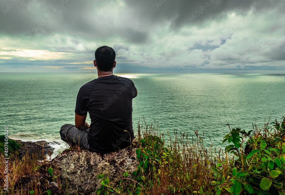man sitting at mountain cliff enjoying the breathtaking view of sea horizon at morning