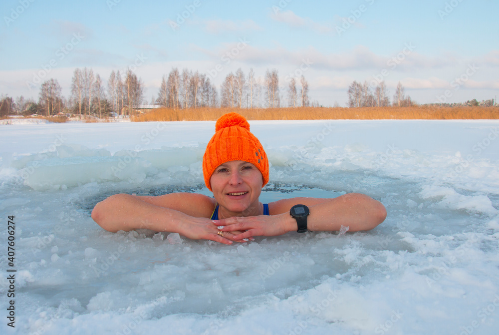 48-year-old woman in an orange hat bathes in an ice-hole in winter, extreme swimming at -25 frost
