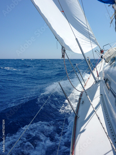 Aboard a sailboat yacht with main sail and genoa sailing fast heeling at a tipping angle on ocean sea.