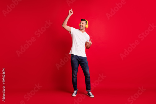 Full length body size photo of smiling millennial listening music in headphones dancing at floor on party isolated vivid red color background © deagreez
